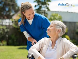 AstraCare caregiving smiling at senior woman in a wheelchair outside.